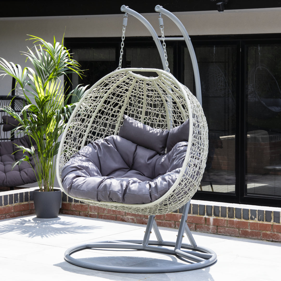 Double Light Grey Rattan Hanging Egg Chair with plush cushions, shown in a garden setting.