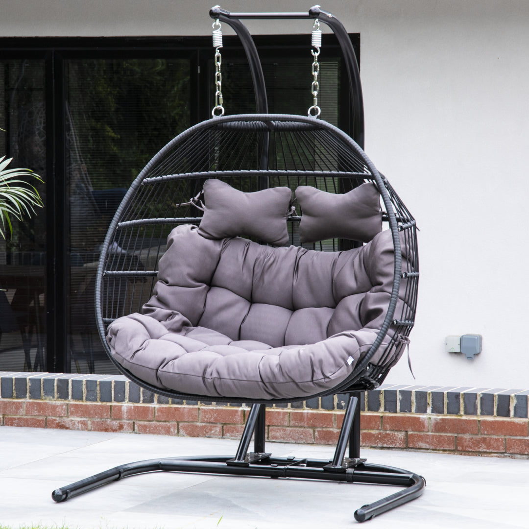 Black double folding rattan hanging egg chair in a sunny garden setting.
